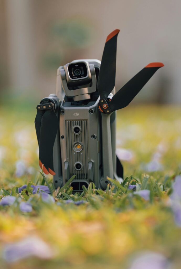 A portable drone resting on a grassy field with flowers, ready for takeoff.